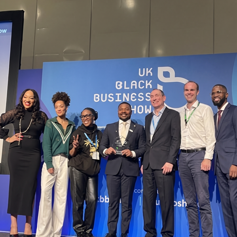 Co-founder of PH247, Louchavan Lemard, celebrating on stage with judges after winning the Lloyds Launchpad Competition at the UK Black Business Show.